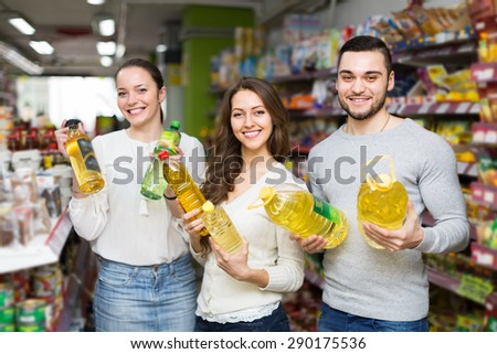 Smiling customers holding seed-oil in plastic packing at shop. Focus on man