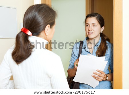 Mature woman answer questions of outreach worker with papers at door in home