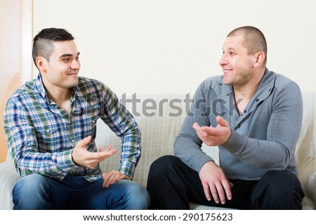 Two male friends sitting on couch and talking at home