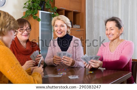 Cheerful smiling elderly female friends playing cards at home