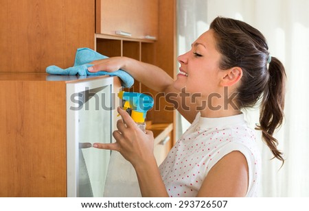 Young brunette woman cleaning furniture at home with atomizer and rag