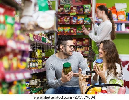 Adults smiling people standing near shelves with canned goods at shop