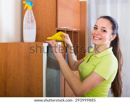 Smiling girl cleaning furniture with cleanser and rag in living room