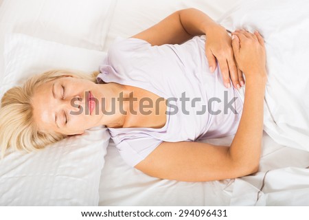 Blonde middle-aged female sleeping on white pillow in bed at home