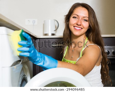 Smiling young female at home kitchen cleaning washing machine