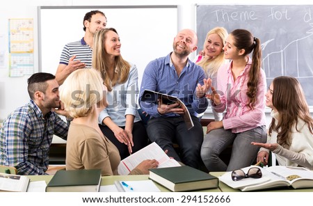 Charming language teacher is telling interesting stories to his attentive students during a break in a classroom