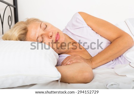 Blonde middle-aged woman sleeping on white pillow in bed at home