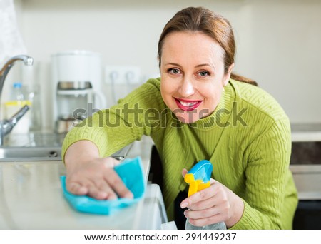 Smiling brunette woman cleaning furniture in kitchen at home