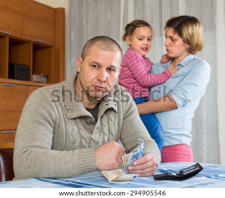 Financial problems in family. Sad woman wit children against husband at table with money