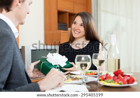 Girl giving present box to man at table during romantic dinner