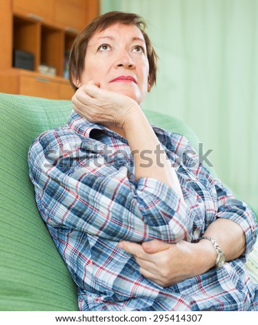 Stressed woman pensioner laying on her elbows and thinking indoor