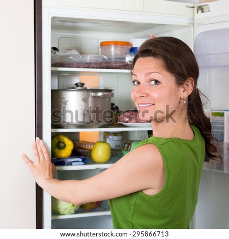 Positive brunette housewife searching for something in refrigerator  at home