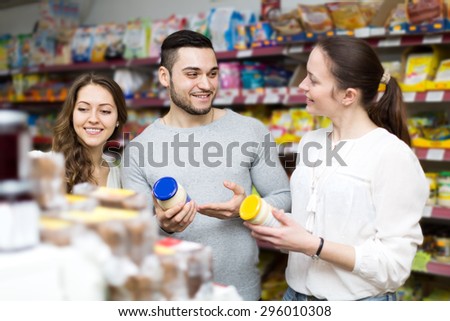 Smiling group of young people to choose canned in grocery store. Focus on the man