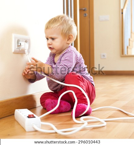 Baby girl playing with electrical extension and outlet on floor at home