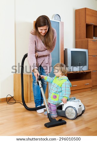 Smiling young mother and baby with vacuum cleaner cleaning living room