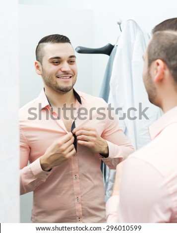 Handsome positive man trying on new shirt at apparel store