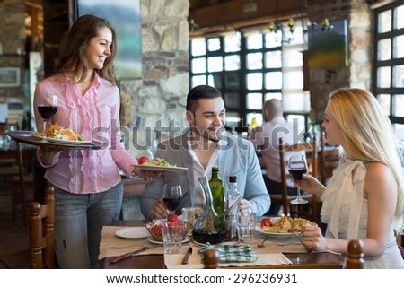 Smiling young brunette female waiter serving restaurant guests. Selective focus