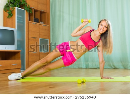 Young slender woman working out with dumbbells at home