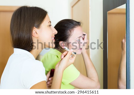 Smiling woman making make-up near mirror. Focus on the left woman