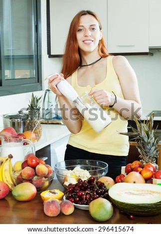 woman making fresh milkshake with blender from fruits and milk at domestic kitchen