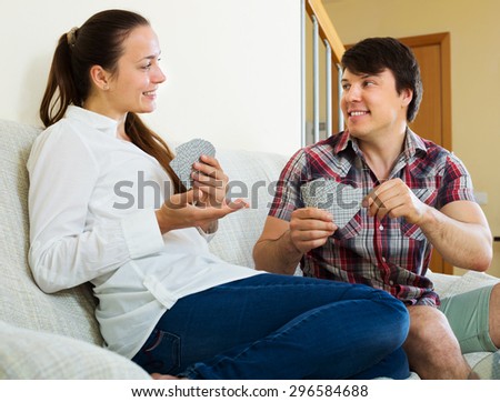 Young smiling couple playing cards and talking sitting on sofa