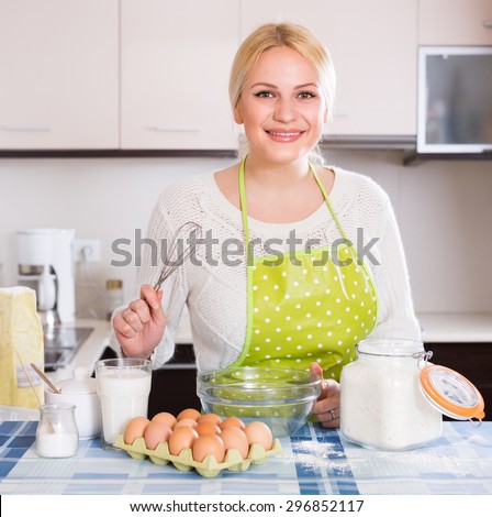 Happy smiling housewife making dough with eggs and milk in kitchen