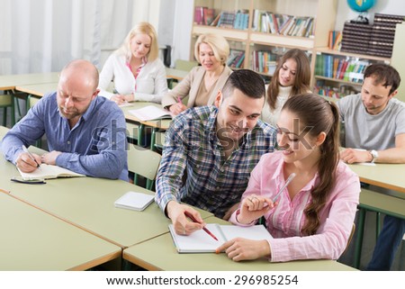 Attentive adult students industriously writing down summary at a classroom
