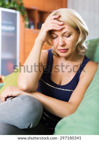 Sad elderly woman sitting on couch at home