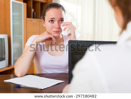 Sad young woman filling questionnaire for employee  of  bank with laptop at table