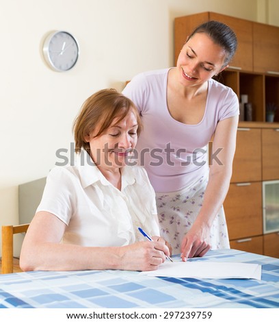 Smiling women signing financial documents at table in home interior