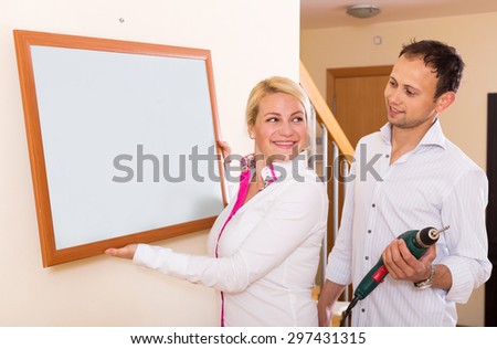 Smiling couple drilling Wall to Hang picture frame at home