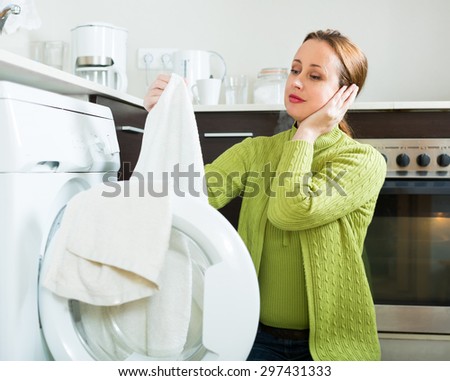 Home laundry. Tired woman in green using washing machine at home