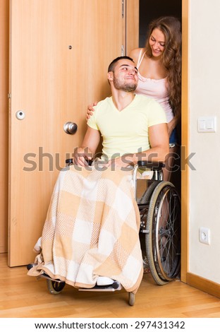 Happy couple with spouse in wheelchair near apartment entrance