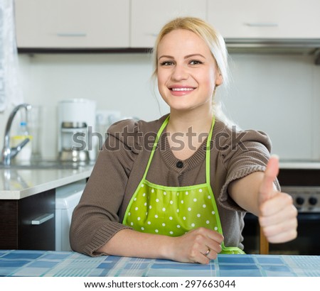 Cheerful young female turned up the thumbs in kitchen
