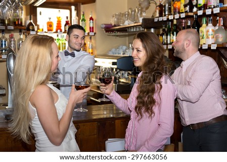 Company of people at a bar: two beautiful women drinking wine while bartender is pouring beer fo a man