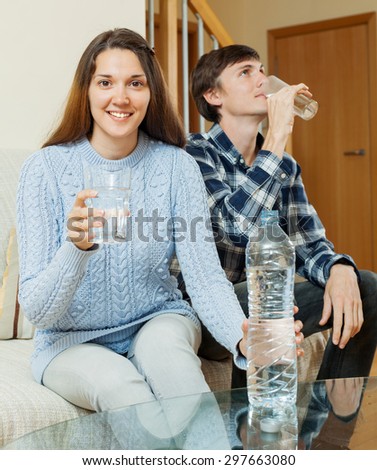 Young couple in home drinking water from plastic bottle