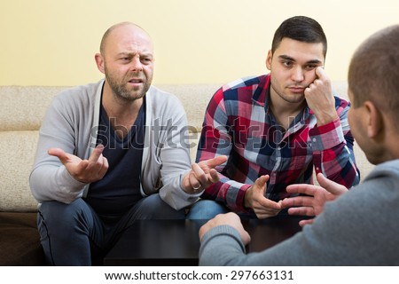 Three adult male friends sitting at the table and sharing the problems