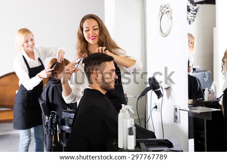 Happy guy cuts hair and female barber at the hair salon. Focus on the man