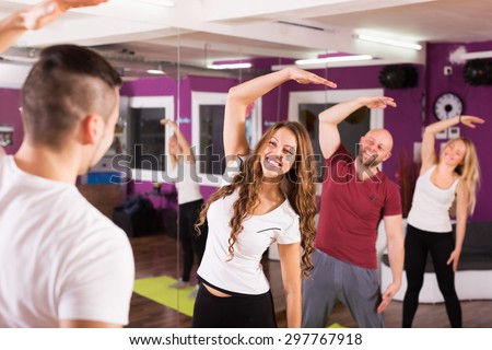 Fitness coach showing to adult happy learners new exercise at class