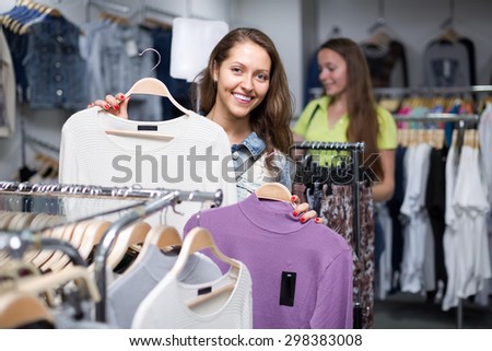 Attractive smiling young longhaired girl choosing pullover in shop