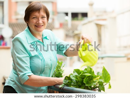 Portrait of aged woman watering domestic plants on terrace