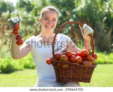Cheerful smiling young woman with tomato harvest in garden