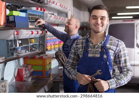 Two workmen standing near storage shelves at auto repair shop