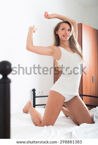 Cheerful long-haired woman  stretching  on bed at bedroom in the morning