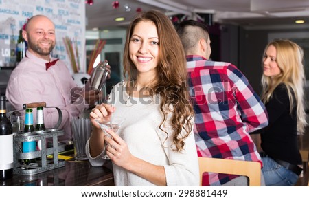 Beautiful smiling woman with a cocktail at a party in a bar. With a bartender and a couple on the background