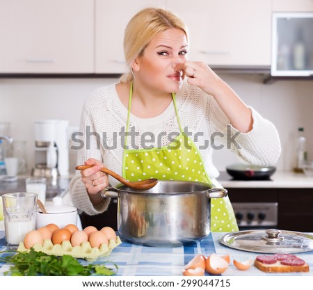 Young woman takes lid off pan and feel musty smell at home kitchen