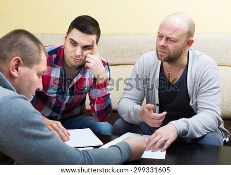Unhappy men sitting at the table with papers and sharing problems