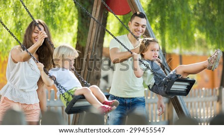 Smiling  mother and father swinging children at park. Focus on woman