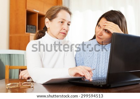 Happy mature woman and her daughter with laptop at table at home