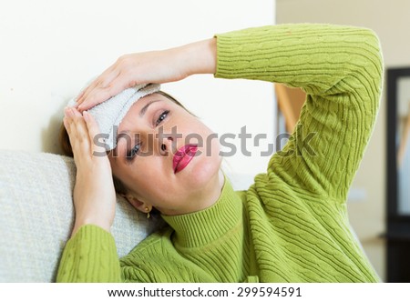 Sick young  woman with huge migraine holding wet towel on her head